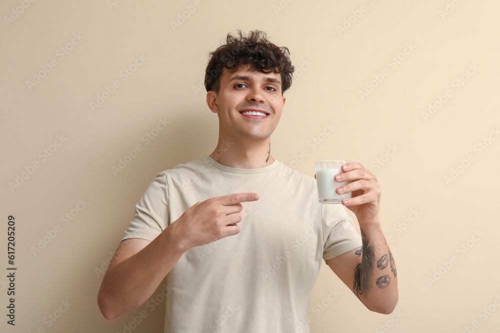 Young man pointing at glass of milk on beige background