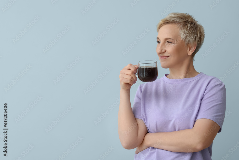 Mature woman with glass cup of coffee on light background