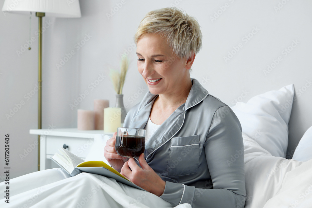 Mature woman with cup of coffee and notebook in bed