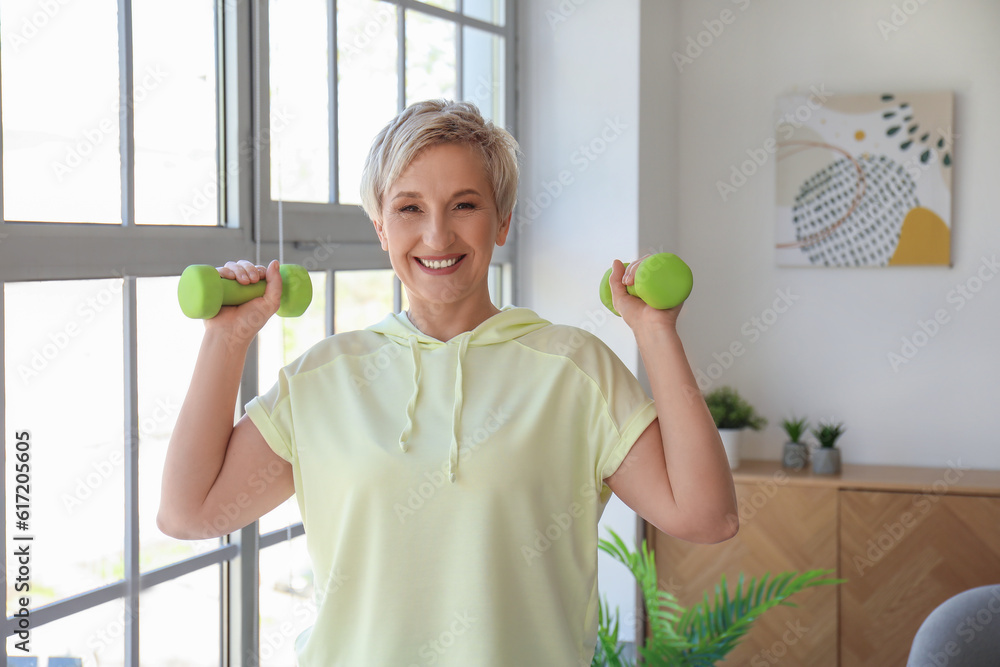 Sporty mature woman training with dumbbells at home