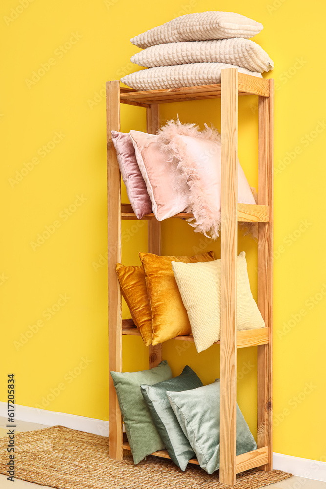 Shelving unit with stylish pillows near yellow wall in room