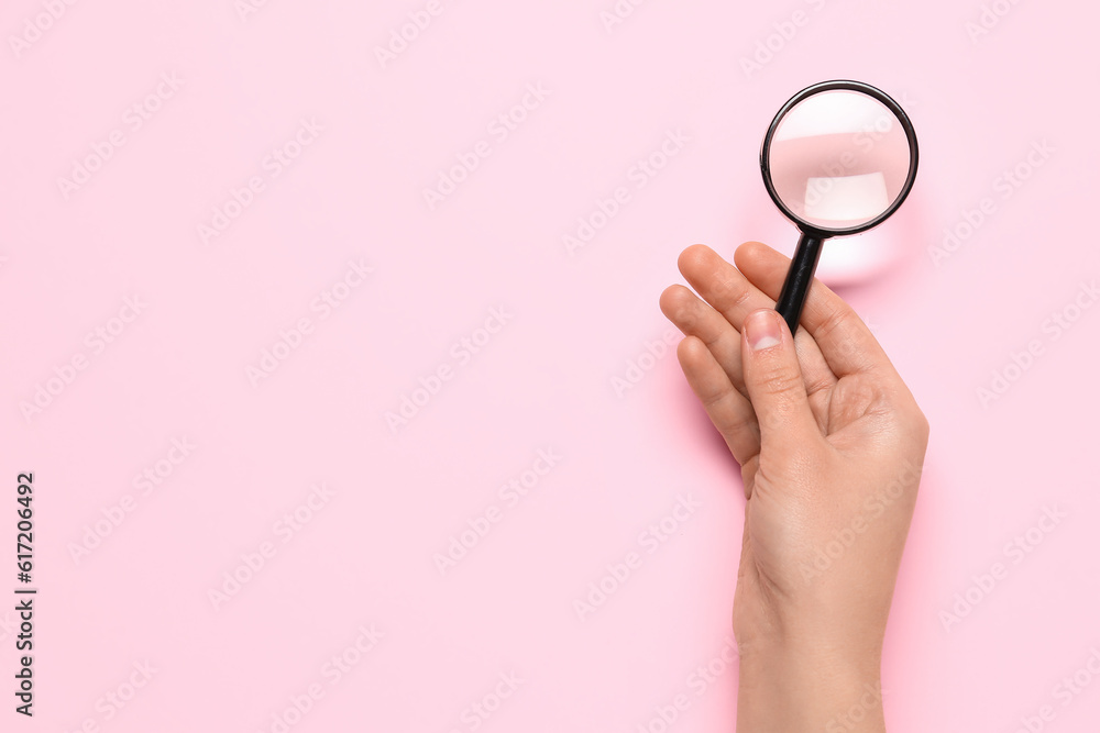 Female hand with magnifier on pink background