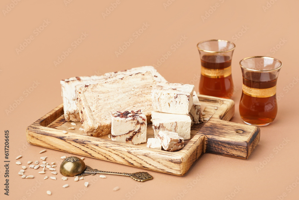 Pieces of tasty marble halva and glasses with Turkish tea on brown background