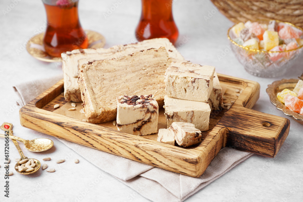 Wooden board with pieces of tasty marble halva on light background