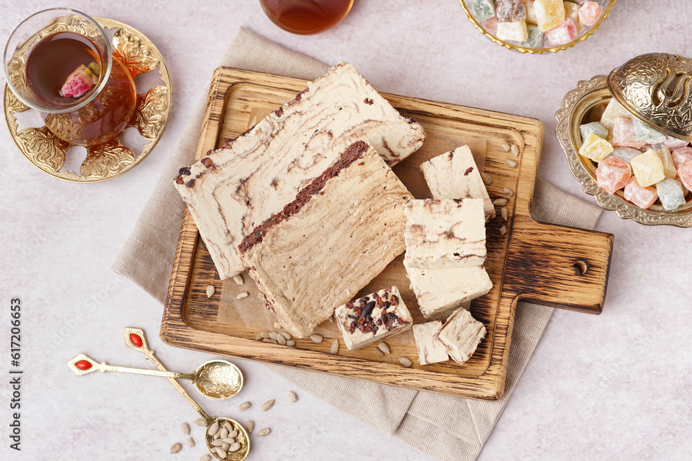 Pieces of tasty marble halva and glass with Turkish tea on white background