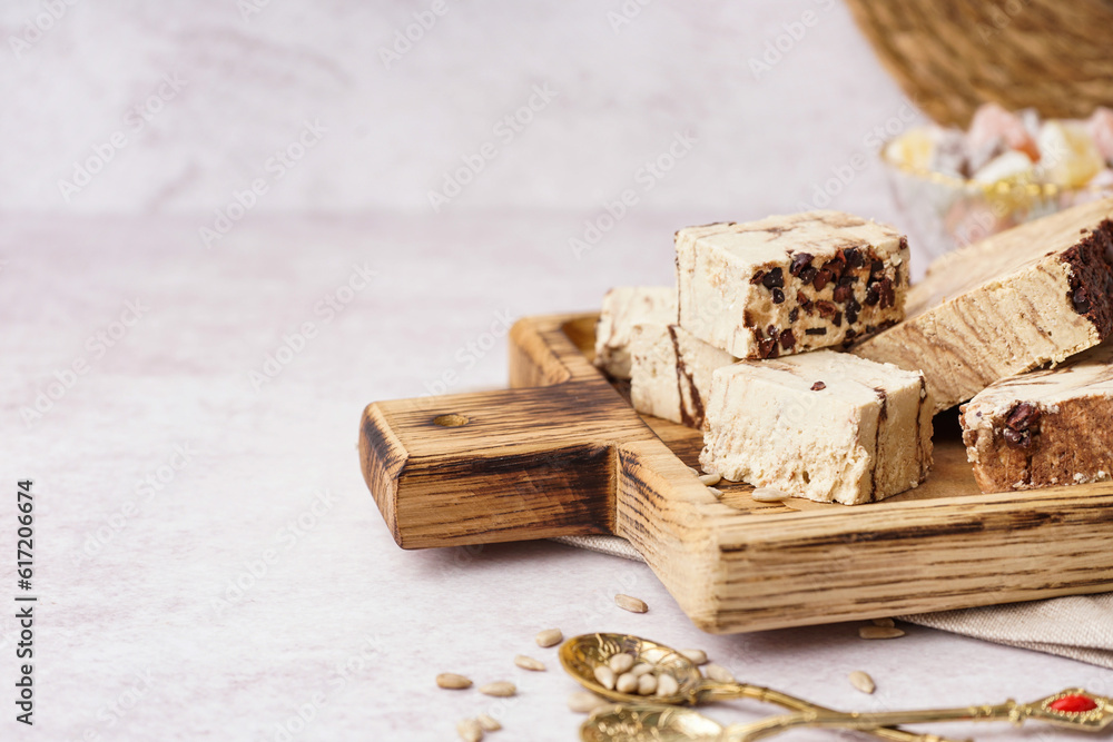 Wooden board with pieces of tasty marble halva on light background