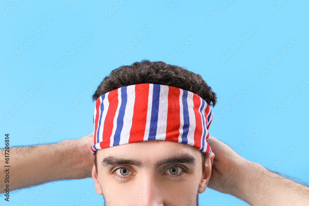 Young brunette man with stylish headscarf on blue background, closeup