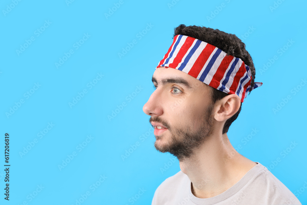 Young brunette man with stylish headscarf on blue background, closeup