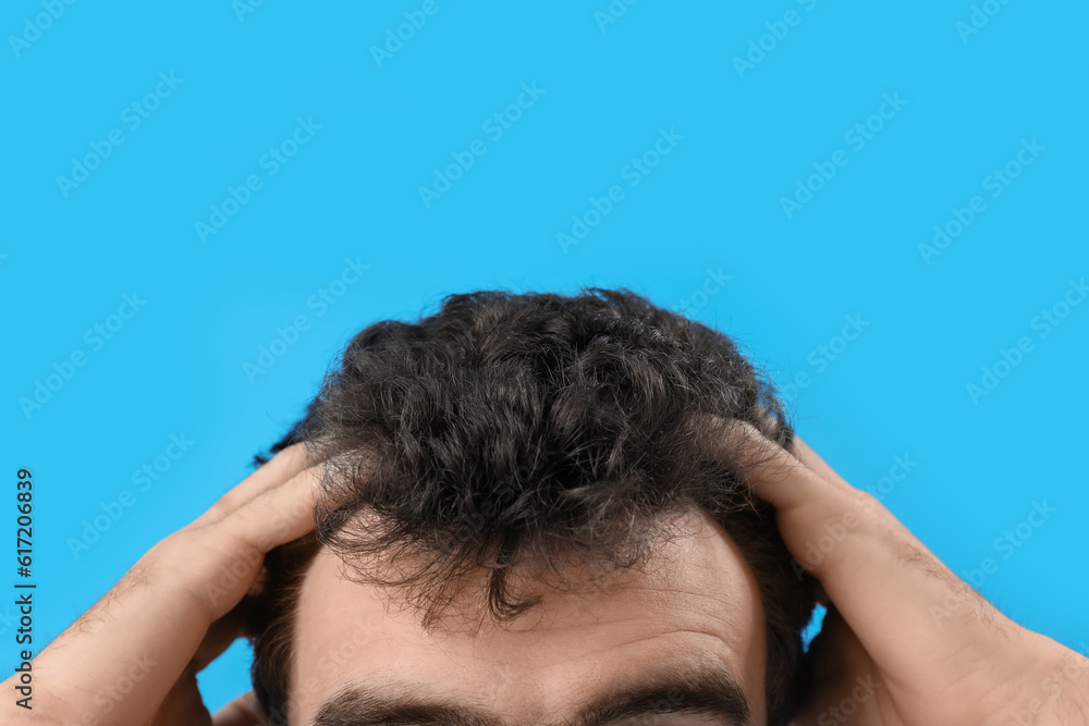 Young brunette man with stylish hairdo on blue background, closeup