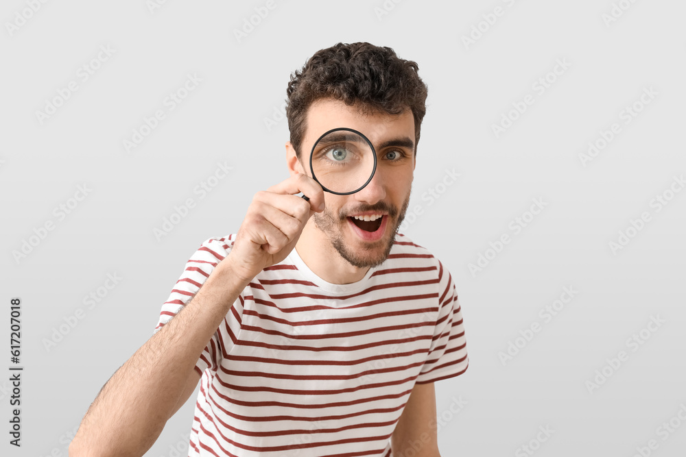 Happy young man with magnifier on light background