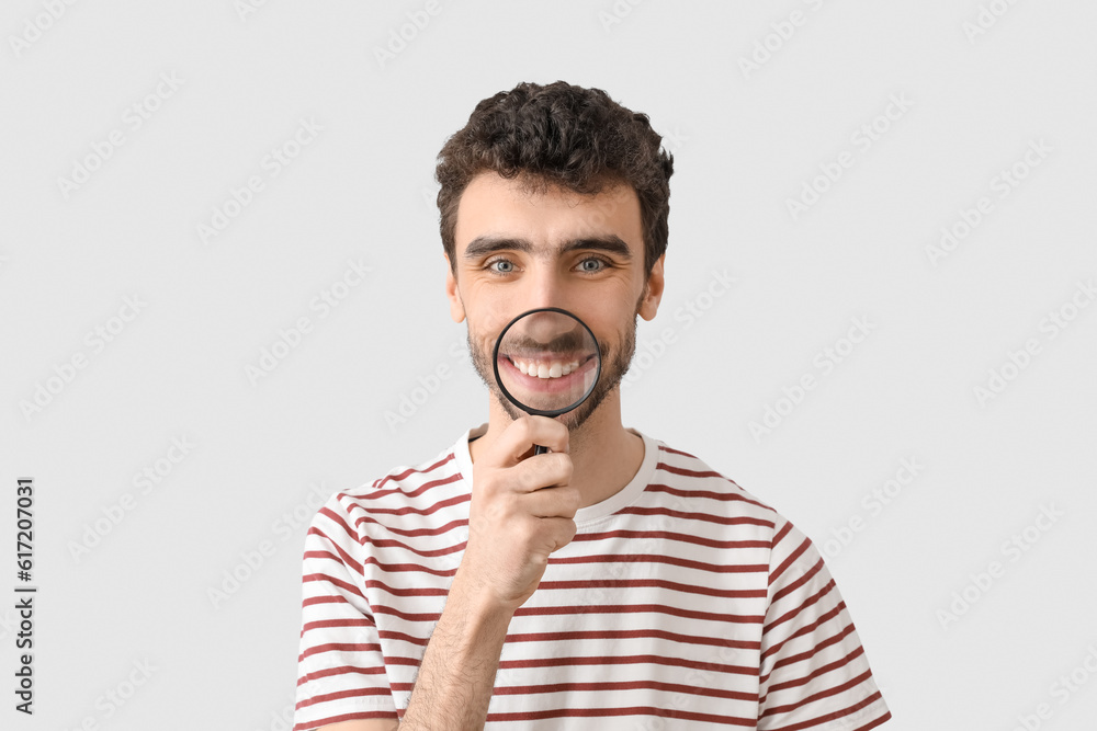 Young man with magnifier on light background