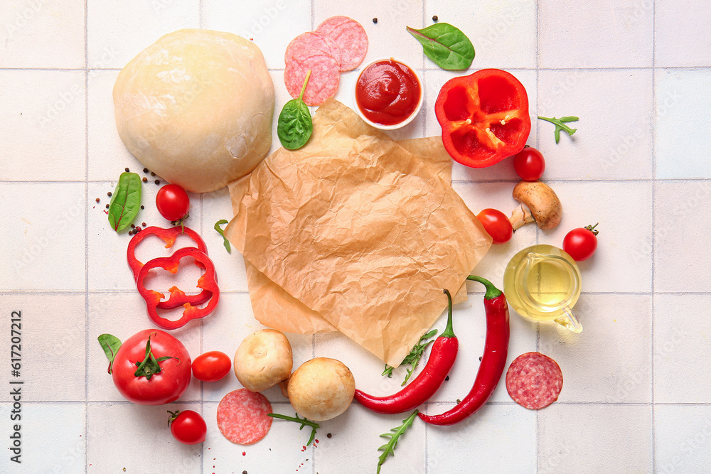 Raw dough with parchment and ingredients for preparing pizza on white tile background