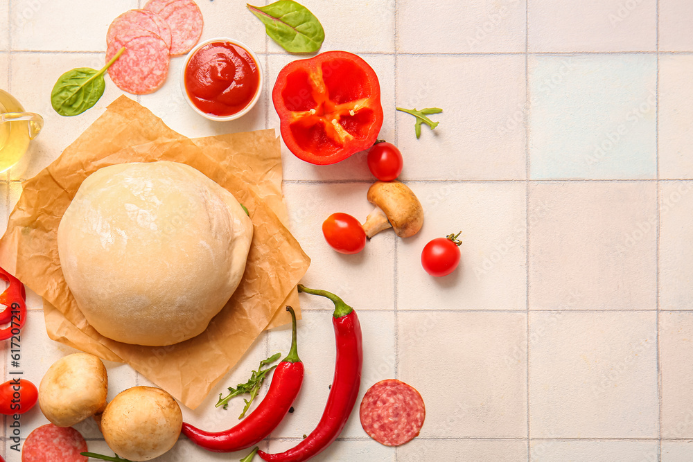 Raw dough and ingredients for preparing pizza on white tile background