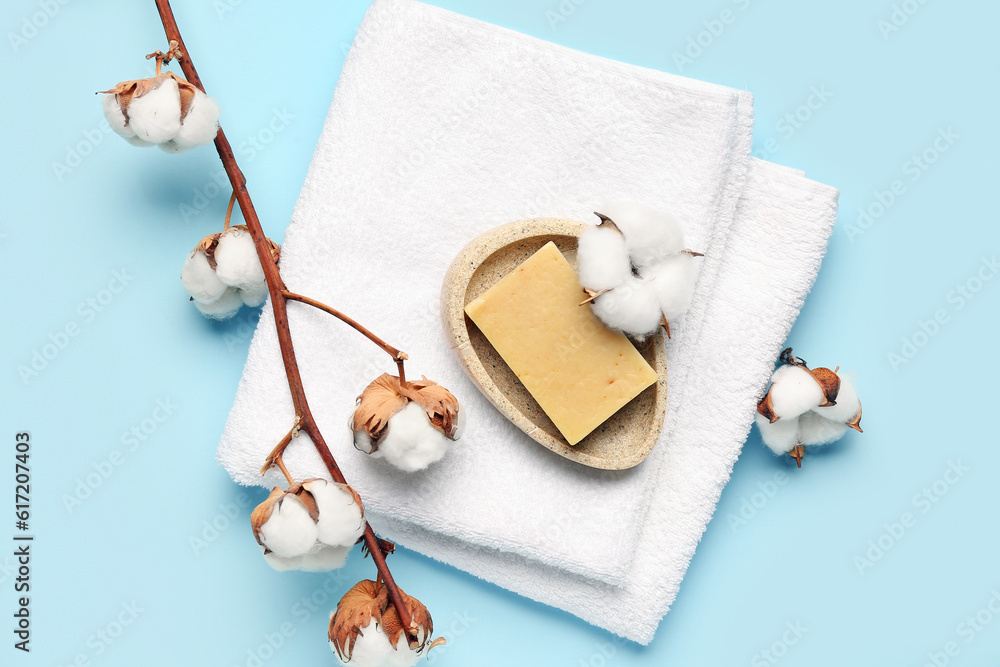 Soap bar, clean towel and cotton branch on color background