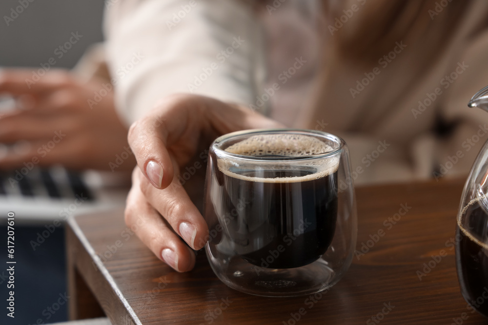 Woman on sofa using laptop and taking cup of coffee from table, closeup