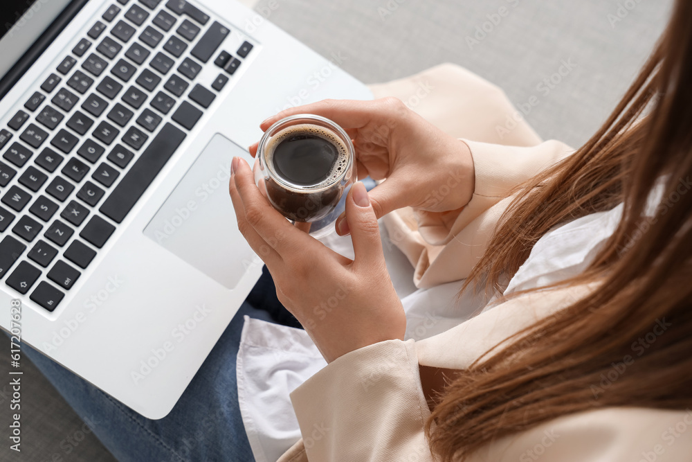 Woman sitting on sofa with modern laptop and glass of delicious coffee