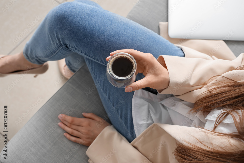 Woman sitting on sofa with glass of delicious coffee