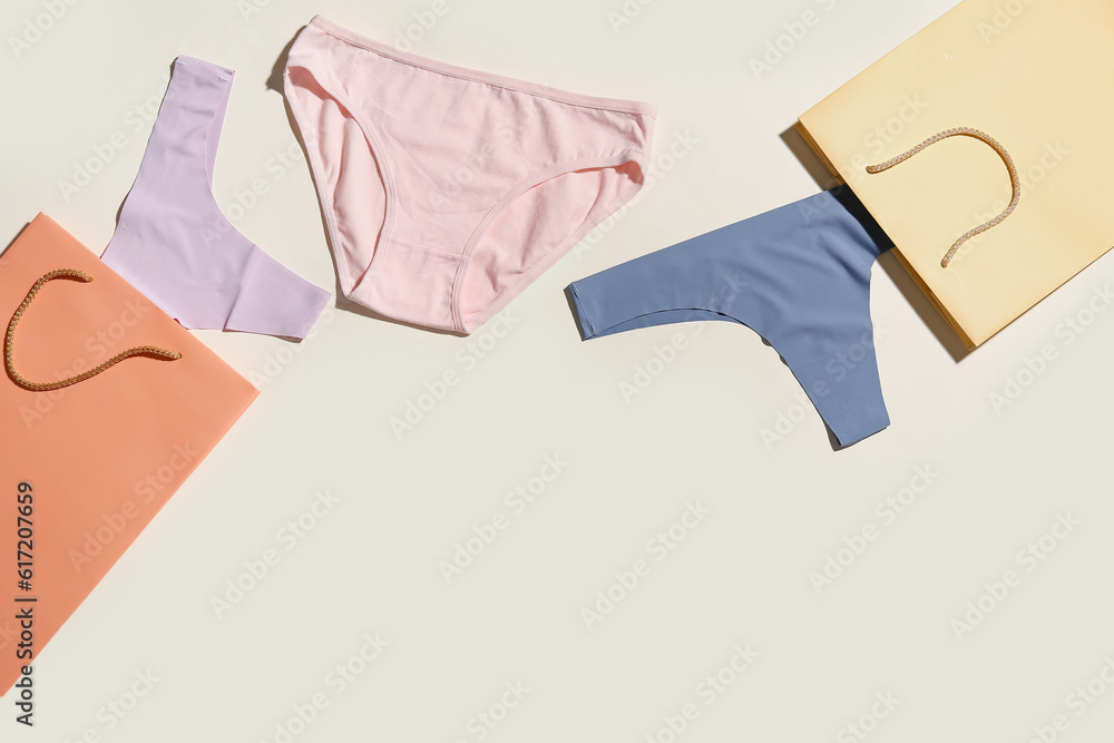 Set of stylish female panties and paper bags on light background