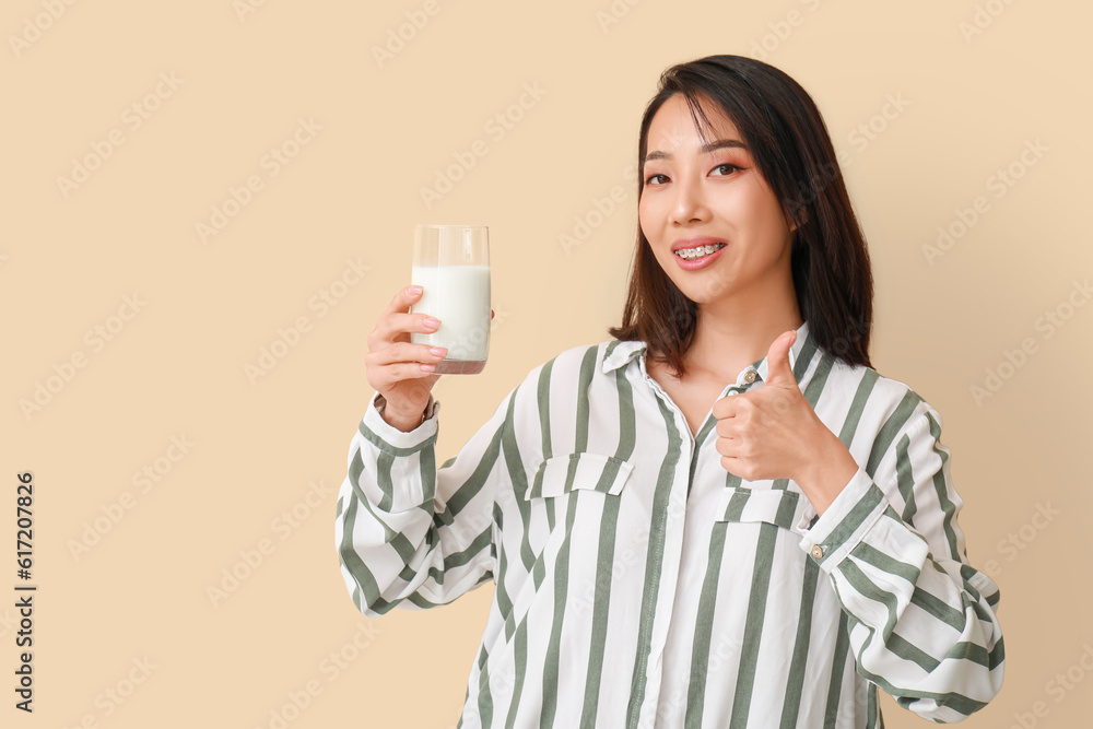 Beautiful Asian woman with glass of milk on beige background