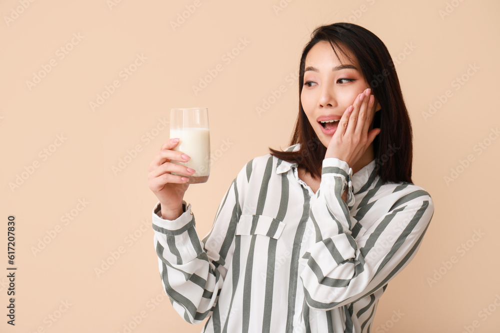 Surprised Asian woman with glass of milk on beige background