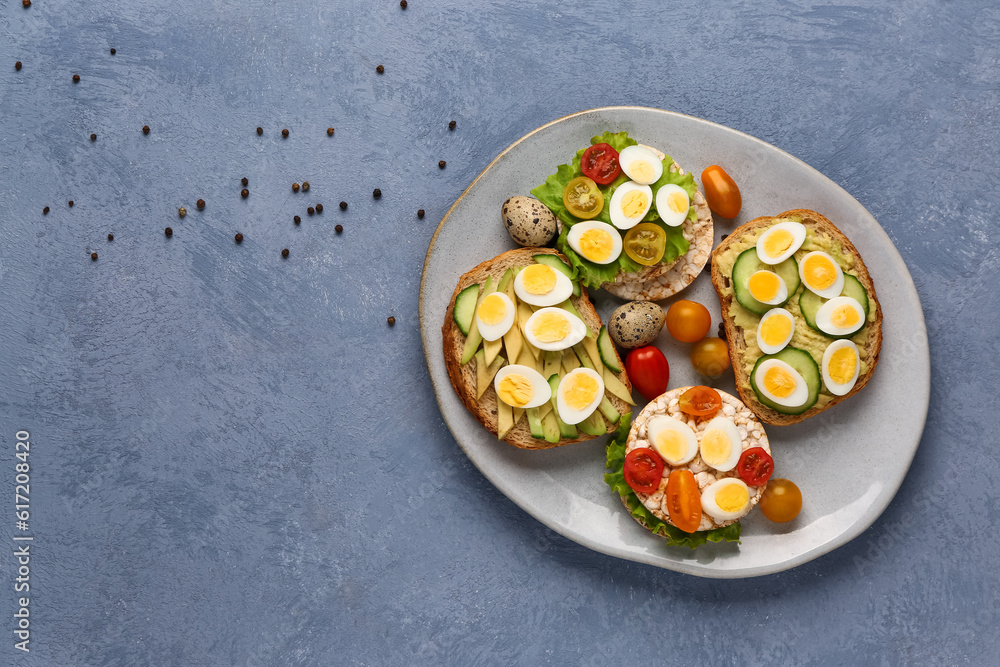 Different tasty toasts with quail eggs, avocado and tomatoes in plate on blue background