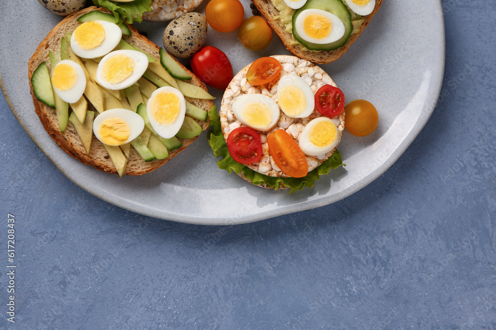 Different tasty toasts with quail eggs, avocado and tomatoes in plate on blue background