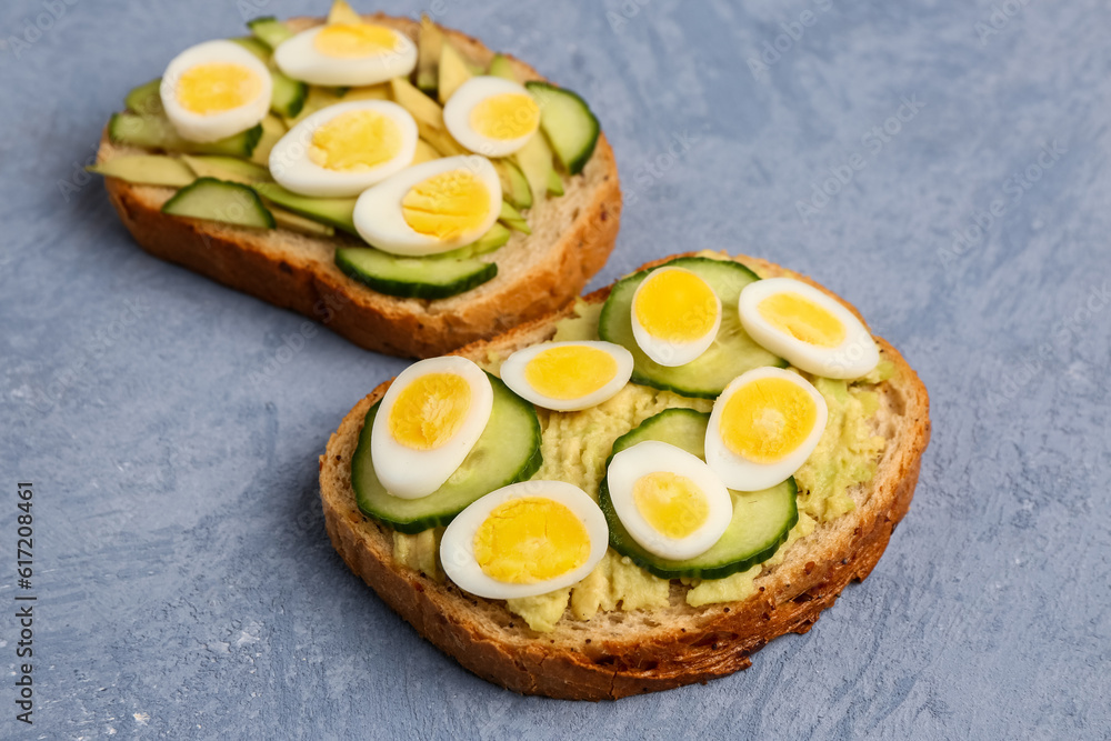 Tasty toasts with quail eggs, avocado and cucumber on blue background, closeup