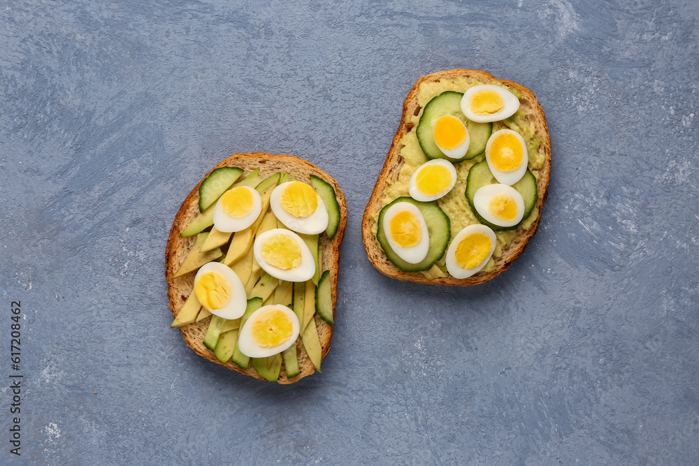 Tasty toasts with quail eggs, avocado and cucumber on blue background