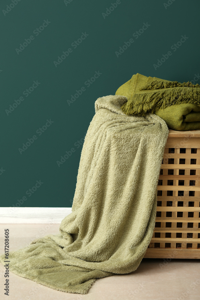 New soft blankets on basket near green wall