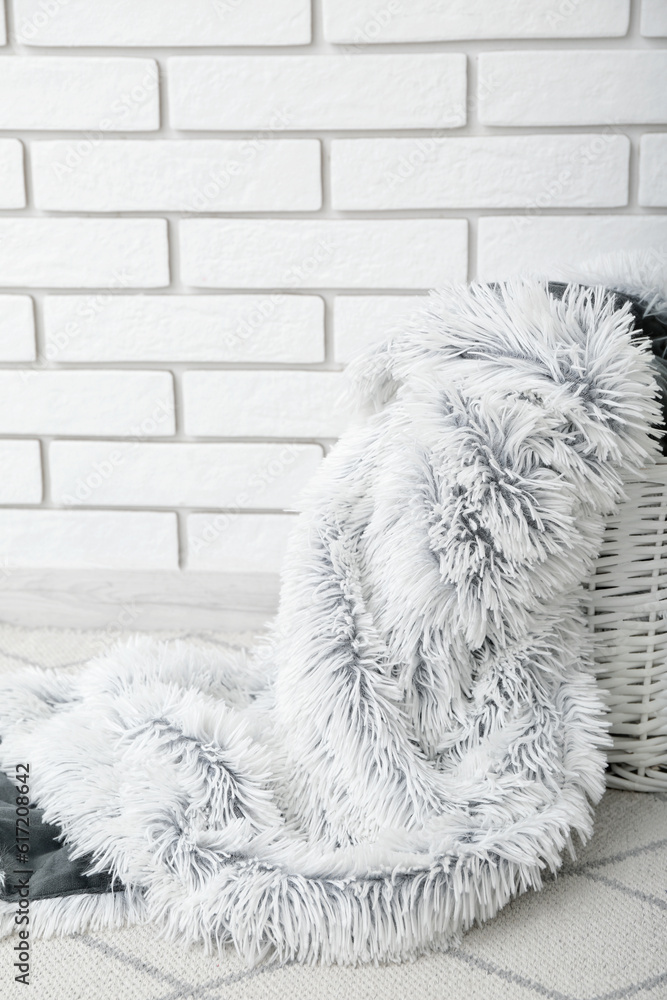 Basket with new soft blanket near light brick wall in room