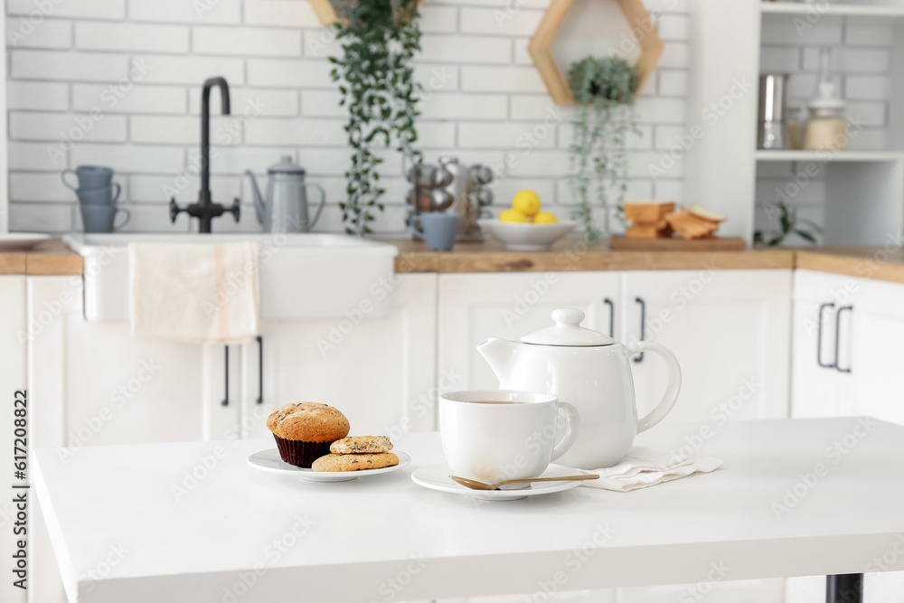 Interior of light kitchen with teapot, cup and snacks on table