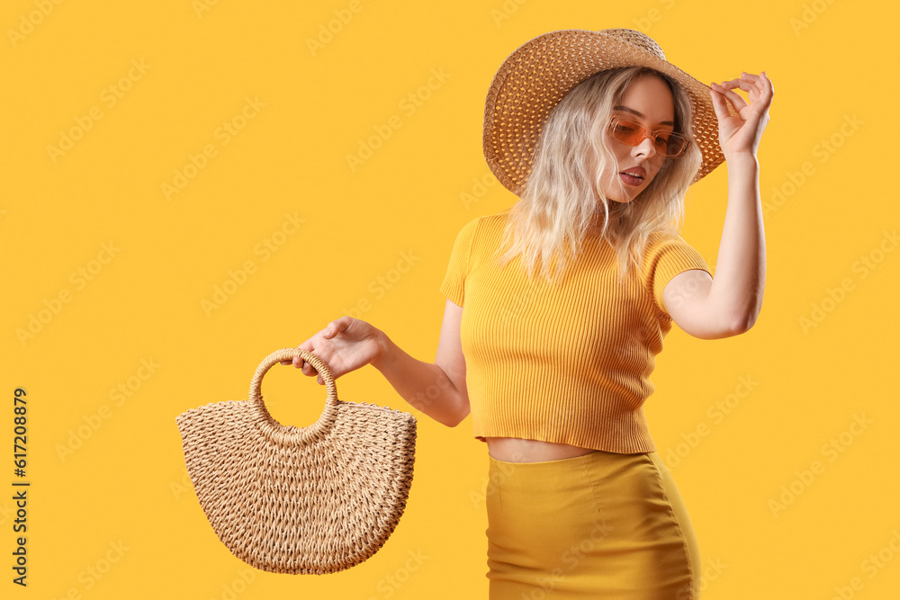 Young woman in stylish sunglasses with bag on orange background