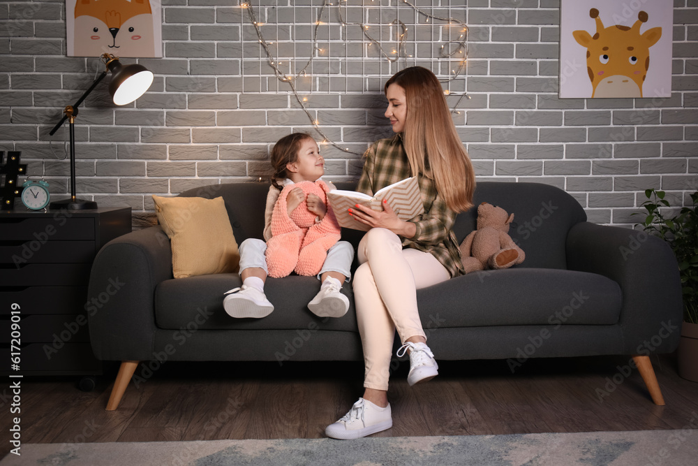 Little girl with her mother reading schoolbook at home late in evening