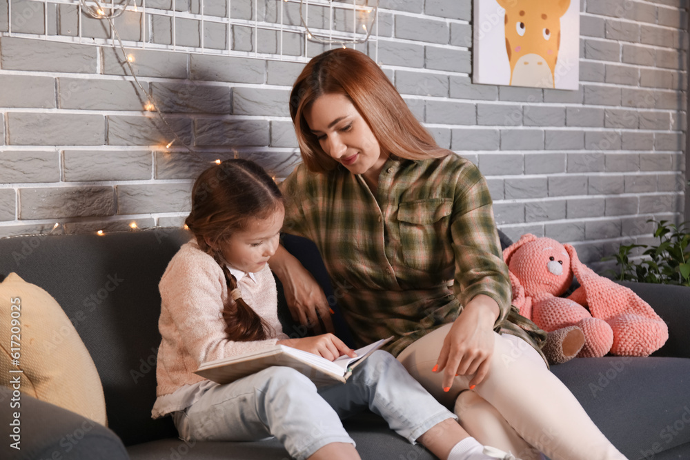 Little girl with her mother reading schoolbook at home late in evening