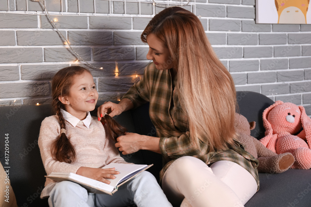 Little girl with her mother reading schoolbook at home late in evening