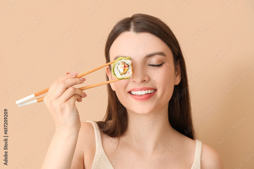 Young woman with sushi roll on beige background, closeup