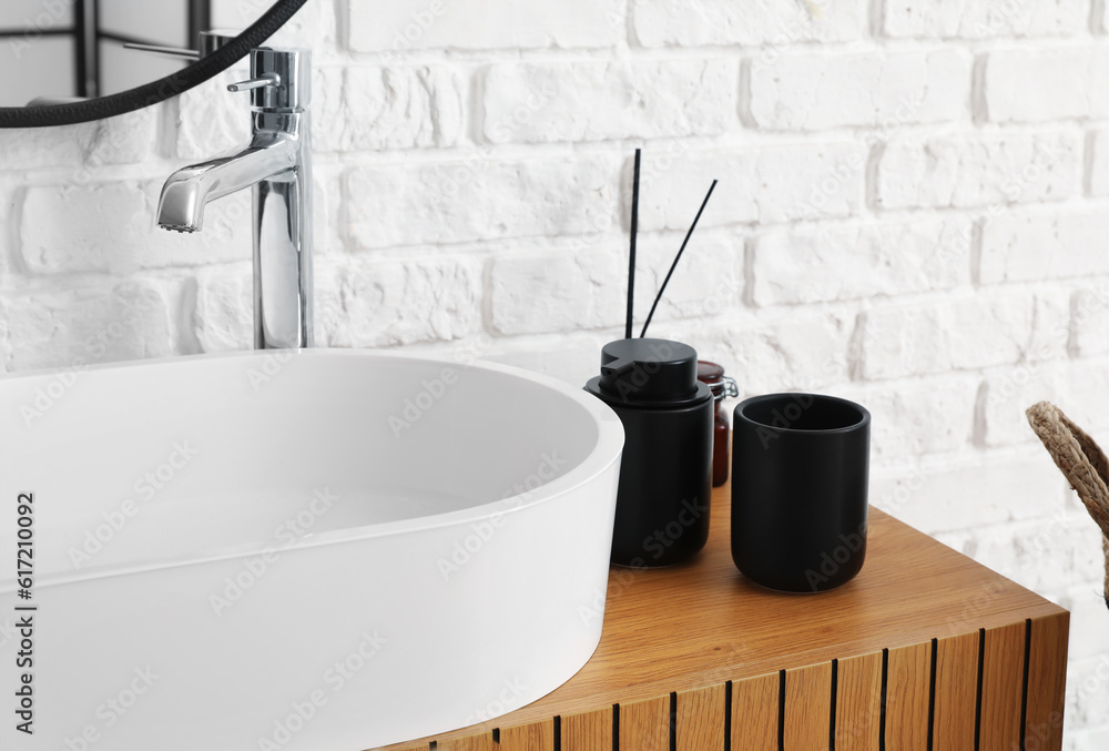 Sink bowl with bath accessories on wooden cabinet in bathroom, closeup