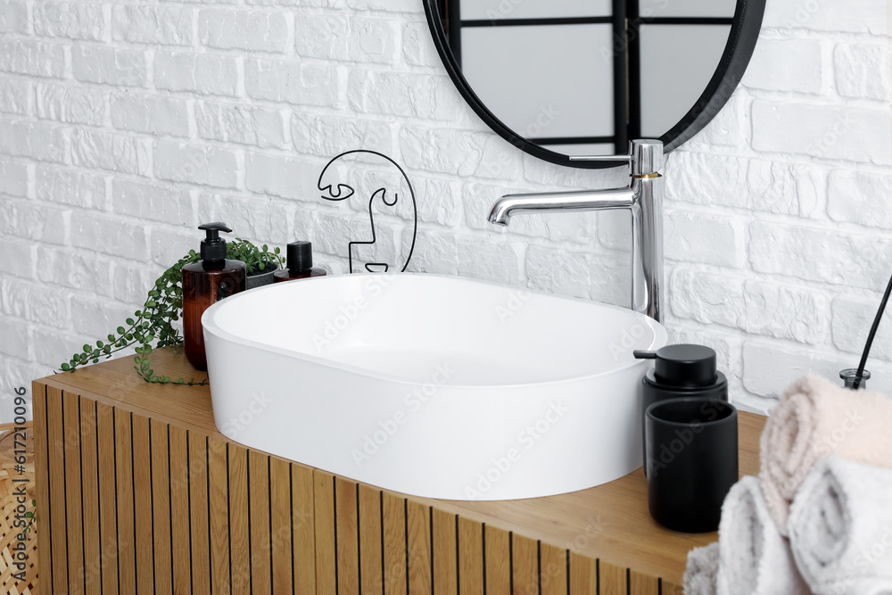 Wooden cabinet with sink bowl, bath accessories and mirror in interior of bathroom