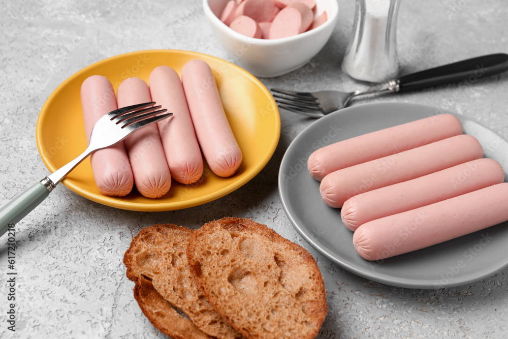 Bowl and plates with tasty thin sausages on grey background