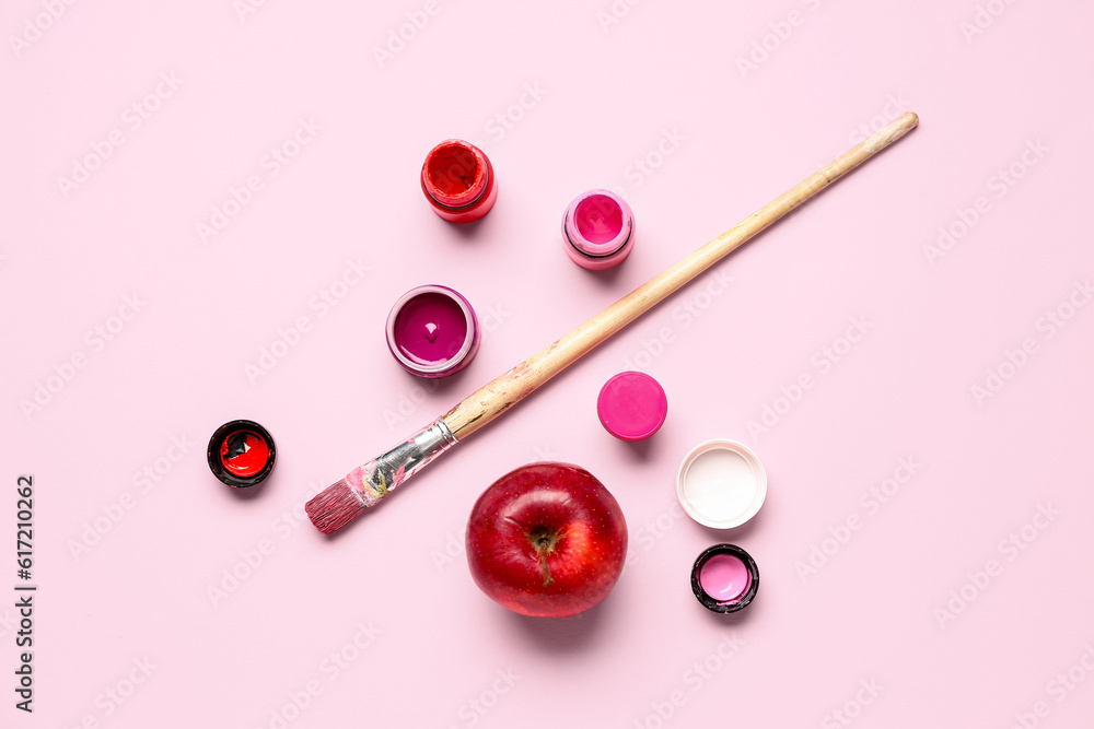 Brush, bottles with different shades of pink paint and apple on color background