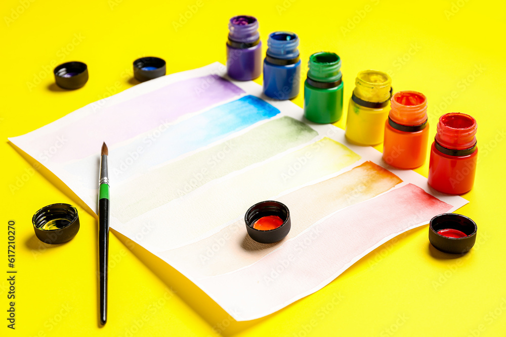 Composition with different paints, brush and rainbow color palette on yellow background