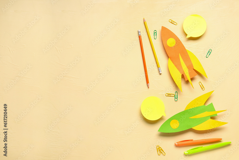 Color paper rockets with pens, pencils and clips on beige background