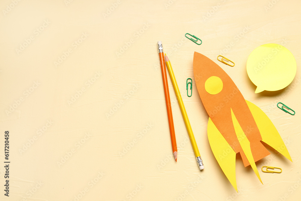 Color paper rockets with sticker, pencils and clips on beige background