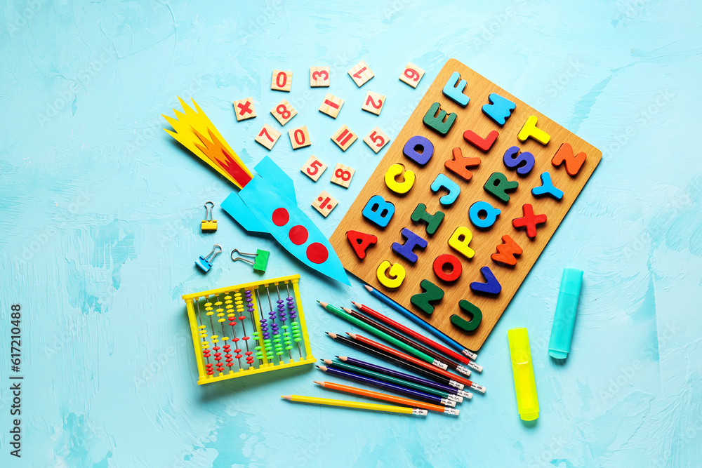 Color paper rocket with abacus, wooden letters and pencils on color background