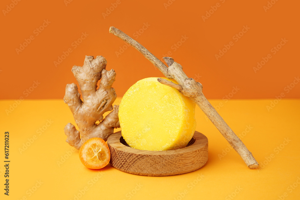 Solid colorful shampoo bar with ginger, branch and kumquat on orange table near wall