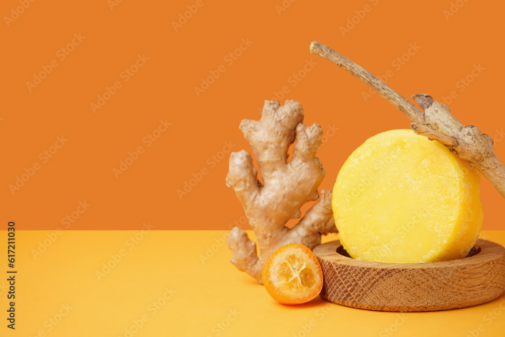 Solid colorful shampoo bar with ginger, branch and kumquat on orange table near wall