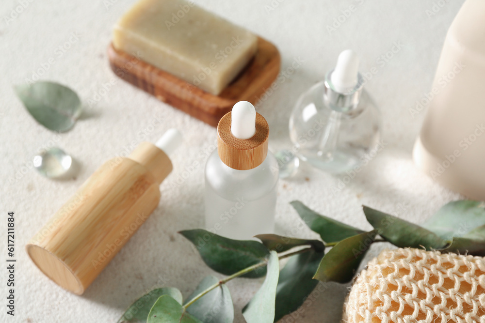 Bottles of cosmetic products, soap and branch on light background, closeup