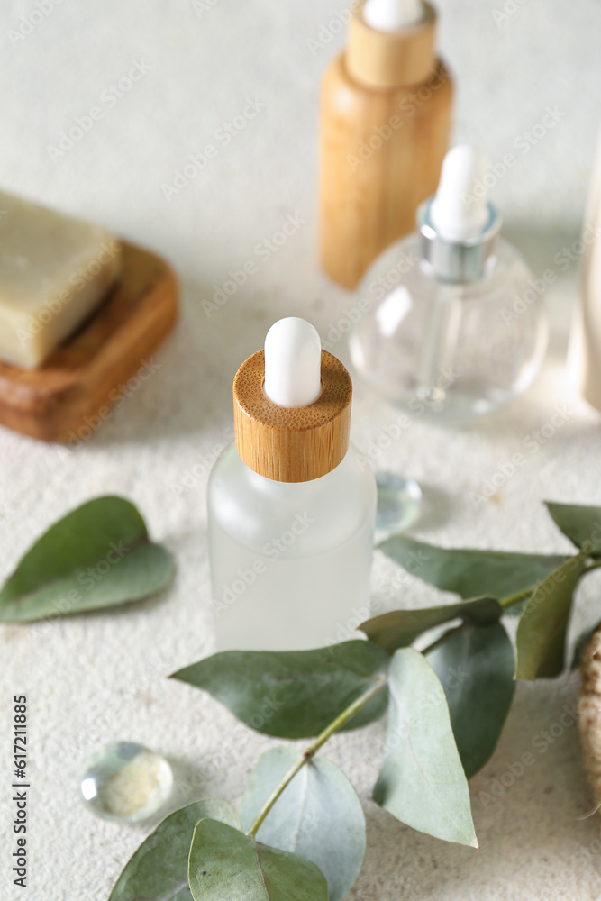 Bottles of cosmetic products, soap and branch on light background, closeup