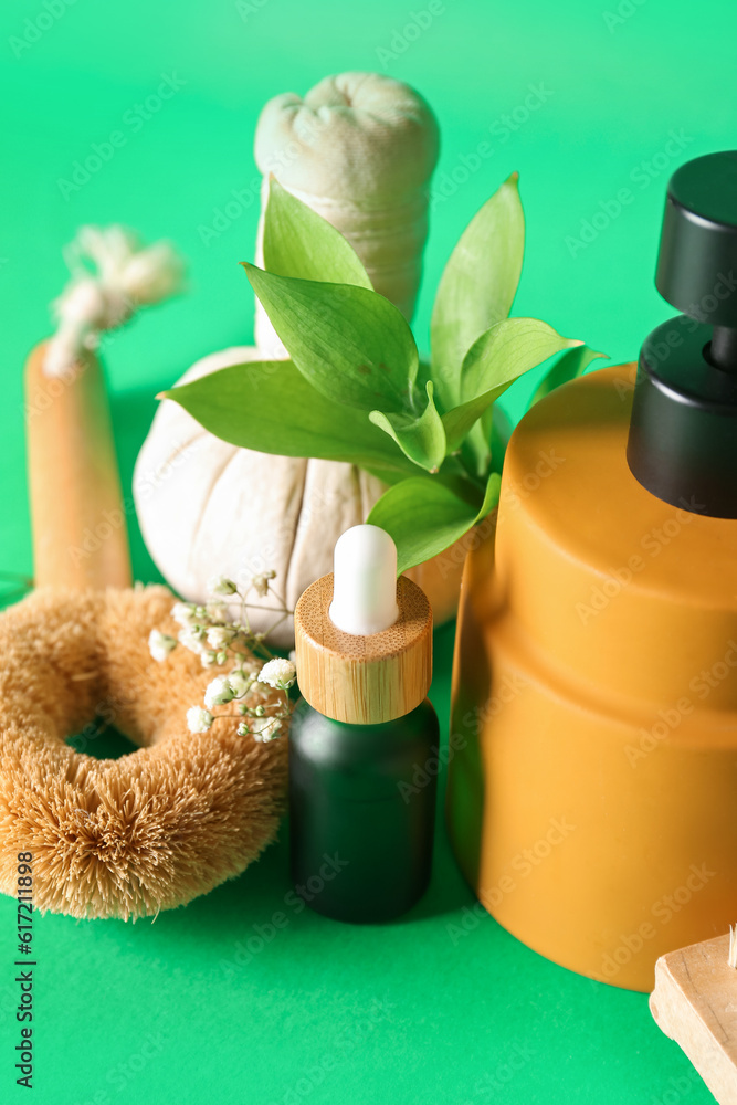 Bottles of cosmetic products, brush, herbal bag and gypsophila flowers on green background, closeup