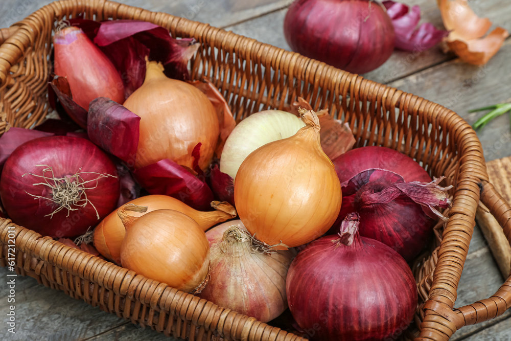 Wicker basket with different kinds of onion on brown wooden background